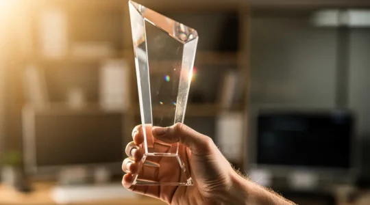 Main tenant un trophée en cristal avec des reflets lumineux symbolisant la reconnaissance professionnelle